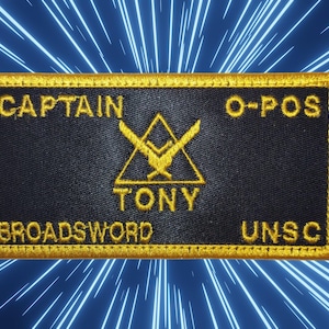 May include: A black and gold embroidered patch with the text "CAPTAIN TONY O-POS BROADSWORD UNSC". The patch features a stylized sword and shield logo.