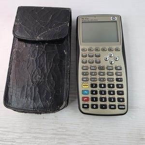 Puede incluir: Una calculadora gráfica HP 49g+ con placa frontal gris claro, teclas negras y pantalla monocromática, junto a un estuche protector rectangular negro y texturizado con cierre de solapa y un pequeño logotipo de HP en relieve.