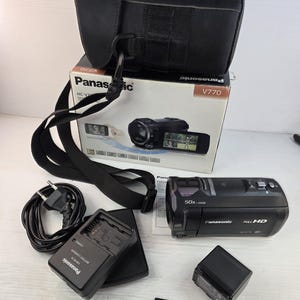 Puede incluir: Una videocámara Full HD Panasonic HC-V770 negra con lente de zoom 50x, acompañada de un estuche negro, un cargador de batería con cable, una batería recargable, una tarjeta de memoria SD SanDisk de 32 GB y la caja original del producto.