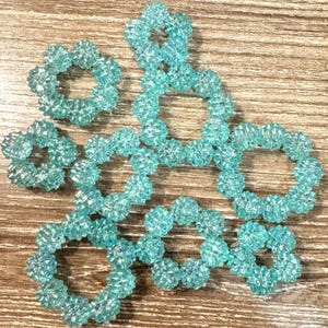 May include: Several clear, light blue beaded rings are arranged on a wooden surface. The rings are made of small, textured beads, and they vary in size and shape. The overall effect is delicate and decorative.