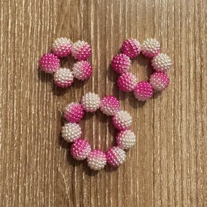 May include: Three pink and white beaded bracelets, each with a different size. The bracelets are made of small, round beads that are half pink and half white.