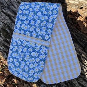 May include: A double oven mitt with a blue daisy floral pattern on one side and a yellow and white gingham pattern on the other. The mitt is made of fabric and has a pocket for the hands.