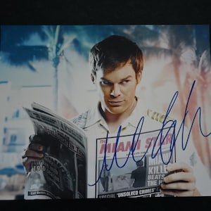 May include: A signed photograph featuring a man holding a newspaper with the headline "Miami Star". The newspaper also displays the text "Killer Beats the Heat" and "Unsolved Crimes". The background shows palm trees and buildings.