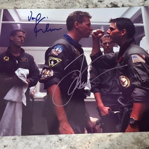 Könnte beinhalten: Ein signiertes Foto von drei Männern in Bomberjacken. Die Männer stehen in einem Raum mit weißen Wänden und einer weißen Tür. Das Foto ist von zwei der Männer signiert, "Val Kilmer" und "Tom Cruise".