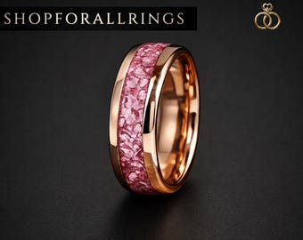 May include: A rose gold ring featuring a central inlay of crushed pink stone fragments. The band has a polished metallic finish. The text SHOPFORALLRINGS is visible in the upper left corner, and a small crown and ring logo appears in the upper right.