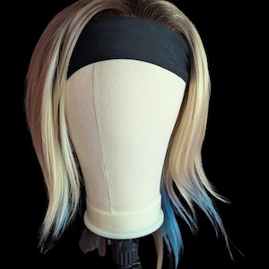 May include: A shoulder-length wig featuring dark brown roots that transition into a light blonde shade, accented with bright blue tips. The hair is styled with a solid black headband worn across the forehead, resting on a neutral-colored mannequin head.