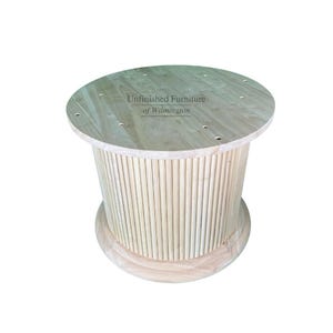 May include: A light-colored, unfinished wooden side table. The round top has several drilled holes and the text "Unfinished Furniture of Wilmington". The cylindrical base is made of vertical wooden dowels, and it sits on a rounded base.