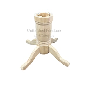 May include: Unfinished wooden table base with three curved legs and a central column. The column has a decorative, turned design and a hexagonal top with holes for attachment. The text "Unfinished Furniture of Wilmington" is visible.