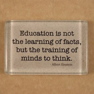Puede incluir: Un pisapapeles de vidrio con fondo blanco y texto negro. El texto dice: "La educación no es el aprendizaje de los hechos, sino el entrenamiento de las mentes para pensar. - Albert Einstein"