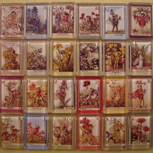 May include: A set of 26 alphabet tiles featuring illustrations of fairies and flowers. Each tile is decorated with a letter of the alphabet and a corresponding fairy and flower design. The tiles are made of ceramic and have a glossy finish.