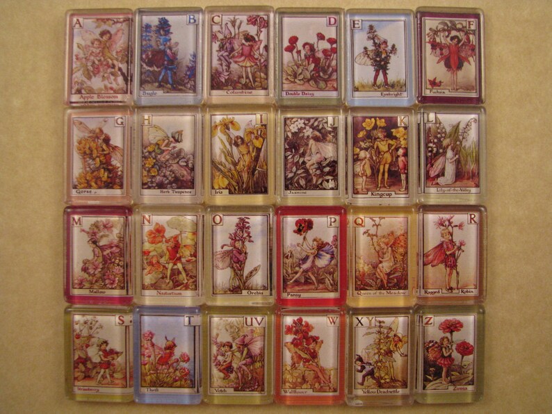 May include: A set of 26 alphabet tiles featuring illustrations of fairies and flowers. Each tile is decorated with a letter of the alphabet and a corresponding fairy and flower design. The tiles are made of ceramic and have a glossy finish.