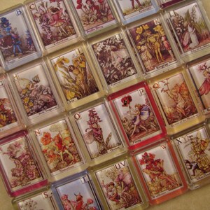 May include: A set of alphabet tiles with colorful illustrations of fairies and flowers. Each tile features a letter of the alphabet and a corresponding image. The tiles are made of glass and have a glossy finish.