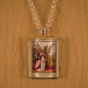 May include: A silver necklace with a rectangular glass pendant featuring a vintage illustration of a fairy with wings and a bouquet of lily-of-the-valley flowers. The pendant has the letter "L" and the text "Lily-of-the-Valley" printed on it.
