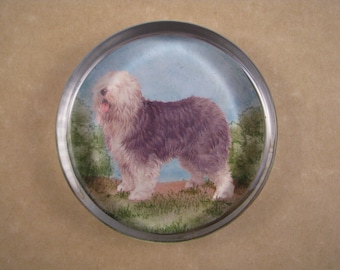 May include: A glass paperweight with a picture of a fluffy, brown and white Old English Sheepdog standing in a grassy field.