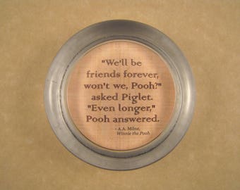 May include: A round, silver-colored metal coaster with a copper-colored center. The center features a quote from Winnie the Pooh, "We'll be friends forever, won't we, Pooh?" asked Piglet. "Even longer," Pooh answered. - A.A. Milne, Winnie the Pooh.