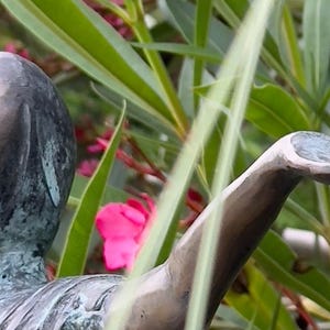 Op de afbeelding: Een bronzen beeld van een persoon met een uitgestrekte arm die een klein gouden model van een gebouw in zijn handpalm houdt.