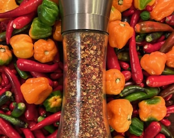May include: A stainless steel pepper grinder filled with a blend of dried red and green peppers. The grinder is surrounded by a variety of red and orange chili peppers.
