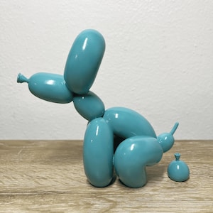 Op de afbeelding: Een tealblauw ballondierbeeld in de vorm van een hond, met zijn staart opgerold. De hond zit in een hurkende positie, alsof hij naar de wc gaat. Er is een klein tealblauw ballonbeeld van een hoop poep naast de hond.
