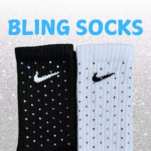 May include: A pair of black and white socks with the text "BLING SOCKS" in blue. The black sock features a white Nike logo, while the white sock has a black Nike logo. Both are decorated with rhinestones.
