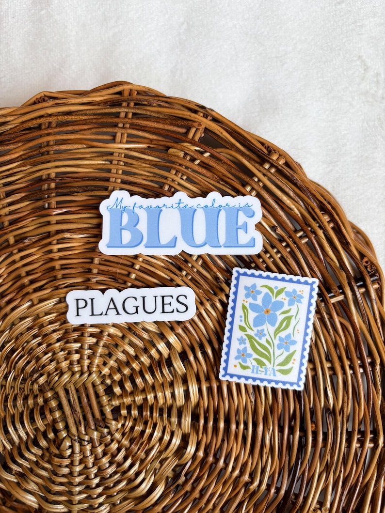 May include: Two stickers on a woven wicker surface. One sticker says "My favorite color is BLUE" in blue text. The other sticker is a blue and green stamp with a floral design and the text "HEYA".