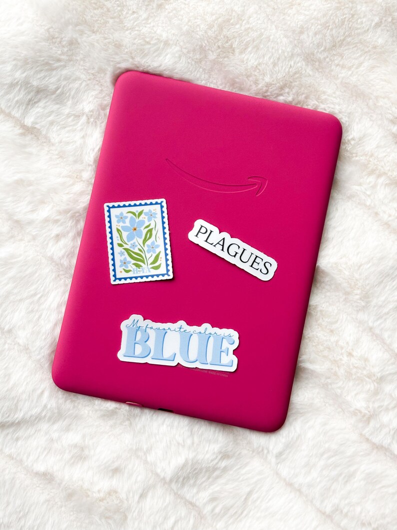 May include: A pink e-reader with three stickers on it. The stickers are a floral design, a sticker that says "My favorite color is BLUE", and a sticker that says "PLAGUES".