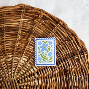 May include: A blue and green floral sticker with a blue border and the text "H-YA" in yellow. The sticker is on a woven wicker surface.
