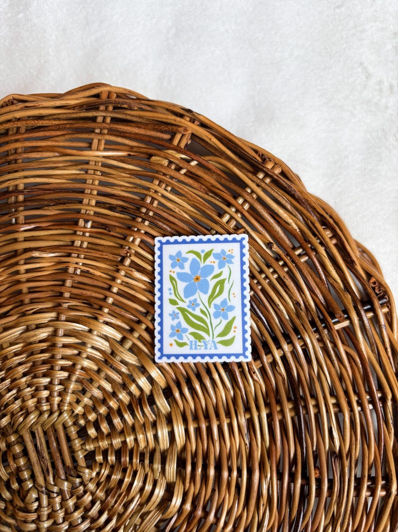 May include: A blue and green floral sticker with a blue border and the text "H-YA" in yellow. The sticker is on a woven wicker surface.