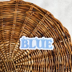 May include: A blue and white sticker with the text "My favorite color is BLUE" on a woven wicker background.