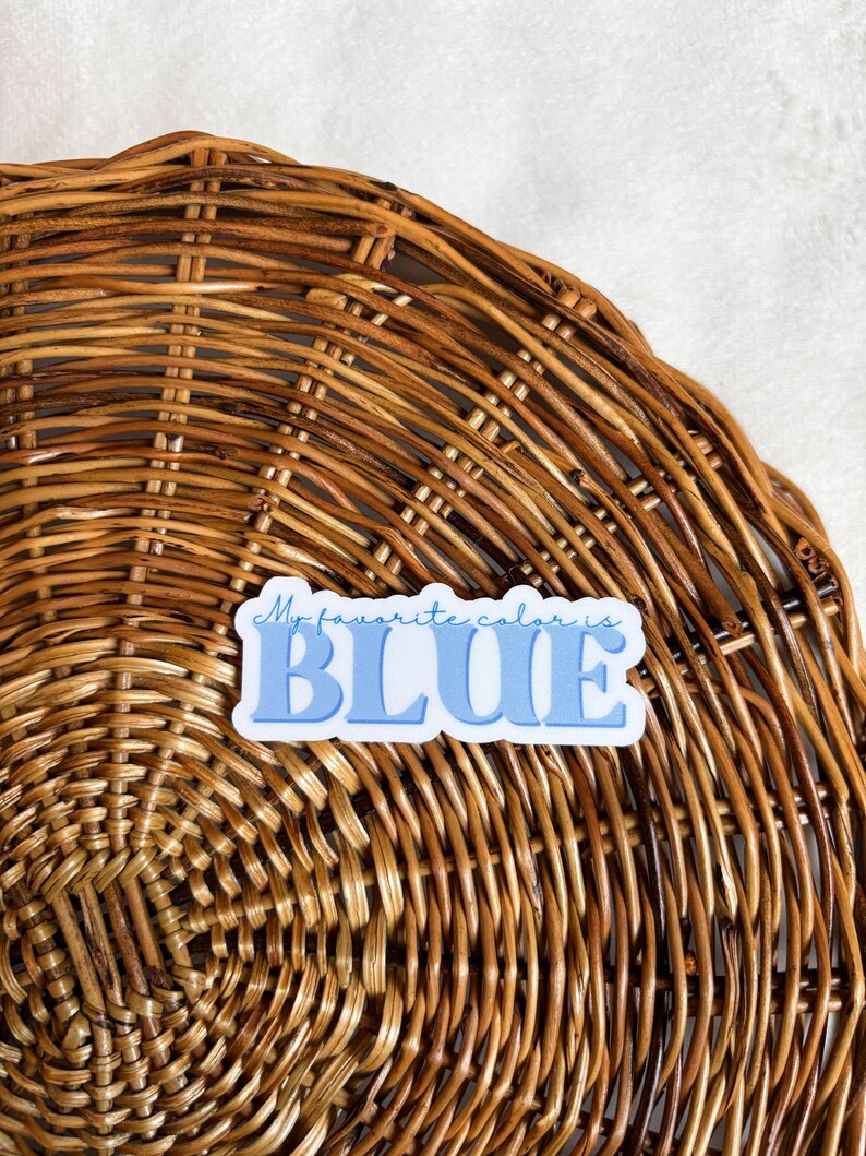 May include: A blue and white sticker with the text "My favorite color is BLUE" on a woven wicker background.
