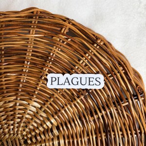 May include: A close-up of a woven wicker basket with a white sticker that says "PLAGUES" on it.