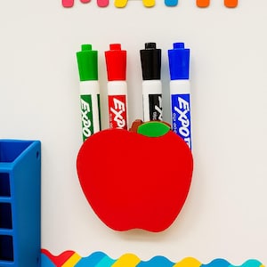 May include: A whiteboard with the word "MATH" in colorful letters, a red apple, and four Expo dry-erase markers. A blue pencil and a blue organizer are also visible. The markers are green, red, black, and blue.