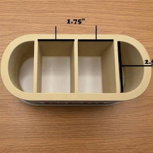 May include: A beige desk organizer with four compartments. The organizer is 1.75 inches wide and 2.5 inches deep. The compartments are rectangular and open at the top. The organizer is made of a light-colored material.