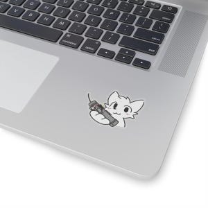 Può includere: Un gatto bianco con le guance rosa che tiene un telecomando grigio e nero.