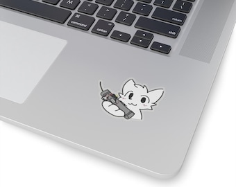 May include: A white cat with pink cheeks holding a gray and black remote control.