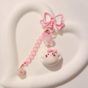 May include: Pink and white charm with a cartoon character face, a pink bow, and a pink beaded chain with a pink bow and a gold key ring.