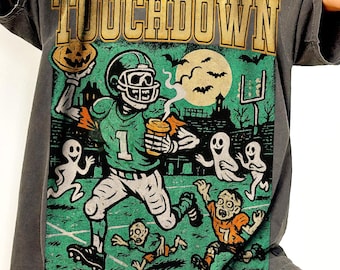 May include: Dark gray t-shirt with a Halloween-themed graphic. The design features a skeleton football player with a pumpkin, ghosts, and the word "TOUCHDOWN" in gold lettering. The background includes a full moon and a football field.
