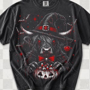 May include: A black short-sleeve t-shirt featuring a graphic of a Highland cow wearing a witch hat, a red bow tie, and holding a jack-o'-lantern filled with candy. The design includes red stars, bats, and glowing red eyes on the cow.