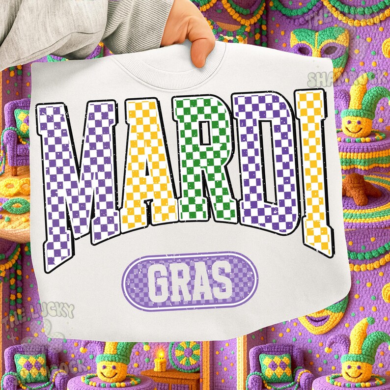 May include: White sweatshirt with the words "MARDI GRAS" in purple, green, and yellow chequered letters. The word "GRAS" is in a purple oval. The sweatshirt is held up by a hand.