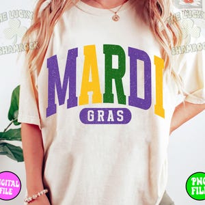 Puede incluir: Una camiseta blanca con un gr&aacute;fico morado, verde y amarillo que dice "Mardi Gras".