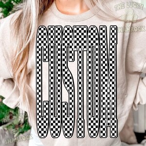 May include: A beige crewneck sweatshirt featuring a large graphic on the front. The graphic consists of the word CUSTOM written in a tall, bold, sans-serif font filled with a black and white checkerboard pattern. The text is centered on the chest.