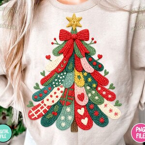 May include: A beige sweatshirt featuring a colorful Christmas tree design. The tree is composed of various knitted elements in red, green, and other colors, adorned with hearts, stars, and bows. A yellow star tops the tree.