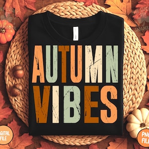 May include: Black t-shirt with the words "AUTUMN VIBES" in orange, green, and white distressed lettering. The shirt is on a woven mat surrounded by fall leaves, pumpkins, and acorns. The shirt is a digital file.
