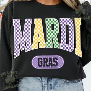 May include: Black sweatshirt featuring the text "MARDI GRAS" in large, checkered letters. The letters are purple, yellow, and green, with a matching checkered oval below that says "GRAS". A festive design for celebrations.