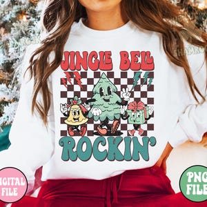 May include: White sweatshirt with a retro Christmas graphic. The design features the text "Jingle Bell Rockin'" with cartoon characters of a bell, Christmas tree, and gift box. The background has a black and white checkered pattern.