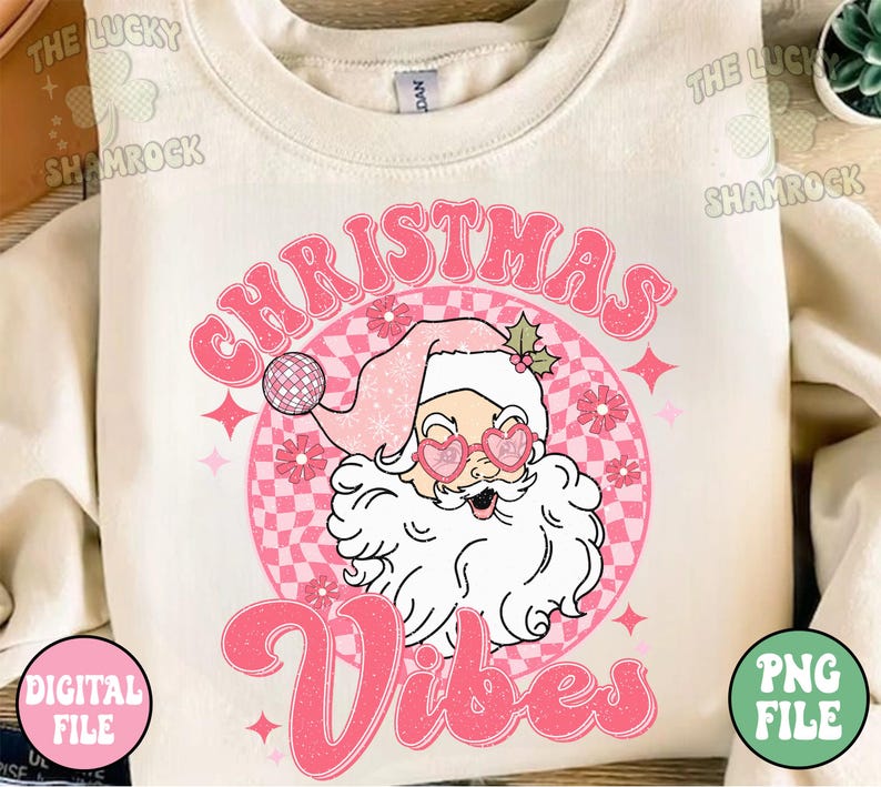 May include: Cream-colored sweatshirt with a retro graphic of Santa Claus wearing heart-shaped sunglasses and a pink Santa hat. The text "Christmas Vibes" is in pink, with a checkered background and star accents. A digital file is available.