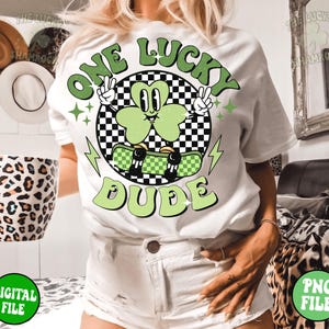 May include: White t-shirt with a green shamrock graphic and the text "One Lucky Dude". The shamrock is wearing a skateboard and has a checkered background.