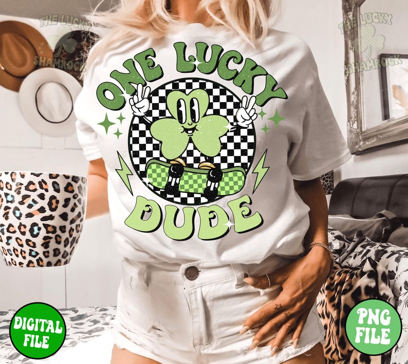 May include: White t-shirt with a green shamrock graphic and the text "One Lucky Dude". The shamrock is wearing a skateboard and has a checkered background.