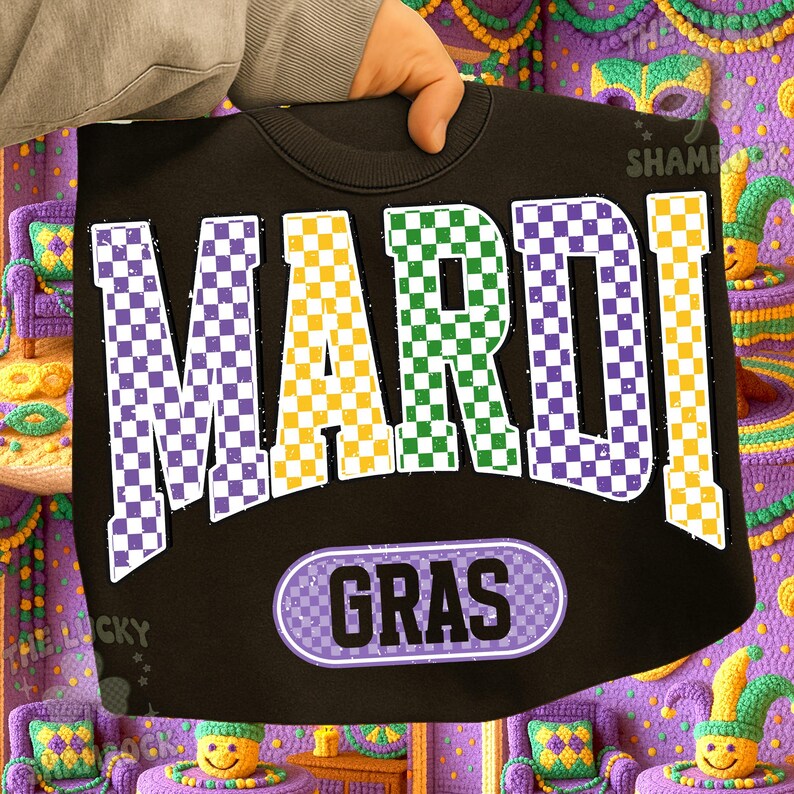 May include: Black sweatshirt featuring the words "MARDI GRAS" in large, checkered letters. The word "MARDI" is in purple, green, and yellow. The word "GRAS" is in a purple oval. The sweatshirt is held by a person.