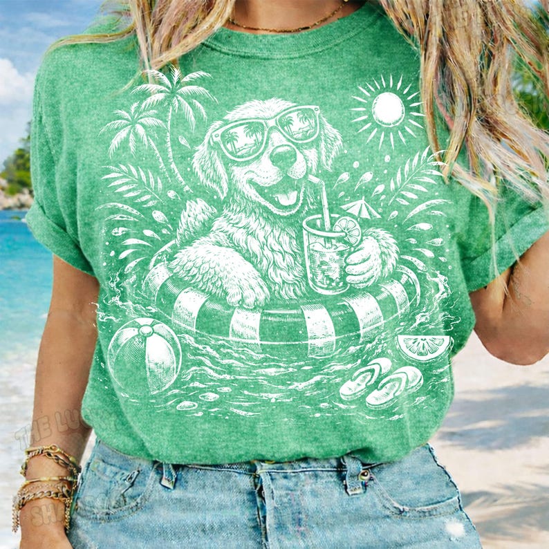 May include: Green t-shirt featuring a white graphic of a dog wearing sunglasses and floating in a pool on an inner tube. The dog is holding a drink with a straw. Palm trees, a sun, and a beach ball are also in the design.