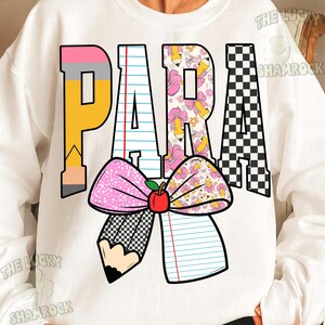 K&ouml;nnte beinhalten: Ein wei&szlig;es Sweatshirt mit dem Wort PARA in gro&szlig;en Blockbuchstaben. Die Buchstaben sind mit Bleistift-, Notizpapier-, Blumen- und Schachbrettmustern gef&uuml;llt. Unter dem Text befindet sich eine gro&szlig;e Schleifengrafik mit einem roten Apfel.